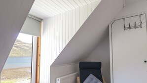 A room with a view of a lake, a chair with a cushion, a radiator, and a white wardrobe with hooks. - Tigh a Phailean (Kyle)