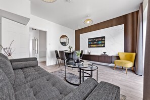 A modern living room with a sectional sofa, a glass coffee table, a dining area with a round table, and a yellow armchair. - Relax & Recharge+Spacious 4BR+Ideal for Families (Greater London)