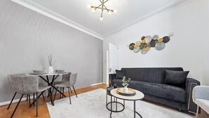 Een moderne woonkamer met een grijze bank, een ronde salontafel en een eethoek met grijze stoelen en een witte tafel.