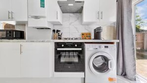 Een compacte keuken met witte kastjes, een ingebouwde oven, een wasmachine en een magnetron.