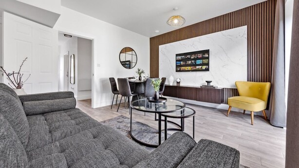 A modern living room with a sectional sofa, a glass coffee table, a dining area with chairs, and a TV mounted on a marble wall. - Fast WiFi & 5 Beds | Group Getaway | Sleeps 7 (Greater London)