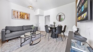A modern living room with a grey sofa, round coffee table, dining table with chairs, and a TV mounted on the wall. - Fast WiFi & 5 Beds | Group Getaway | Sleeps 7 (Greater London)