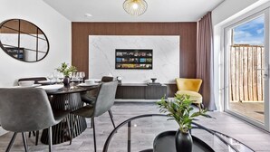 A modern dining area with a round table, grey chairs, and a black vase with green plants. - Fast WiFi & 5 Beds | Group Getaway | Sleeps 7 (Greater London)