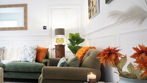 Ein Wohnzimmer mit einem grünen Sofa, einem kleinen Tisch mit einer Kerze und einer Vase mit orangefarbenen Blumen.