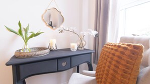 Ein Zimmer mit einem dunkelblauen Konsolentisch, einem Spiegel, einer Vase mit weißen Blumen, einer Kerze und einer Pflanze.