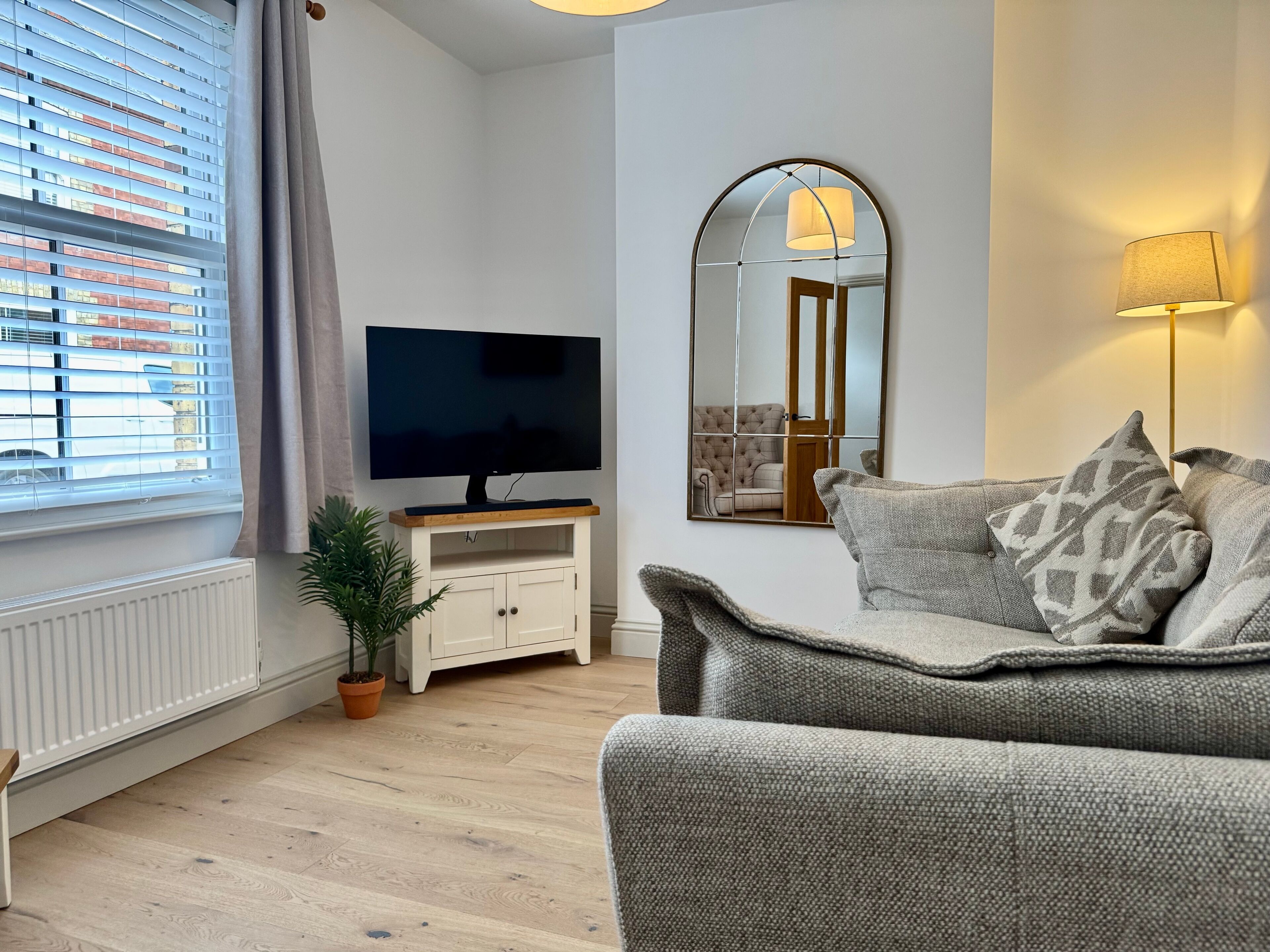 A modern living room with a flat-screen TV, a sofa, a mirror, and a lamp.
