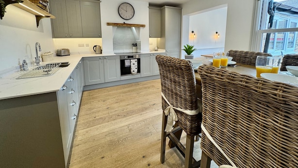 Une cuisine moderne avec des meubles gris, un îlot central et un coin repas doté de chaises en osier.