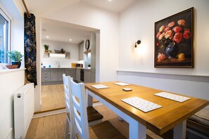 Un comedor con mesa y sillas de madera, un cuadro de flores en la pared y una cocina al fondo.