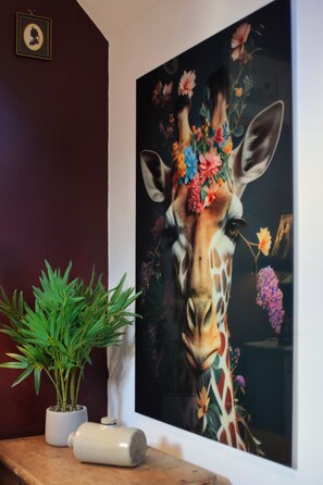 A framed painting of a giraffe with flowers on its head, a potted plant, and a decorative object on a wooden surface. - The Loft - 1 BR in the Heart of Stamford, Burghley (Lincolnshire)
