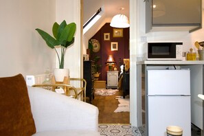 A compact living space with a sofa, a dining area with a table and chairs, a kitchen with a microwave and refrigerator, and a hallway leading to a bedroom. - The Loft - 1 BR in the Heart of Stamford, Burghley (Lincolnshire)