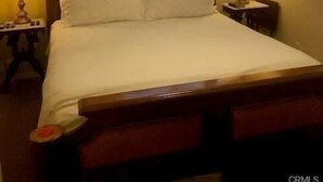 Een slaapkamer met een bed, twee nachtkastjes met lampen, een plafondventilator en een raam met jaloezieën.