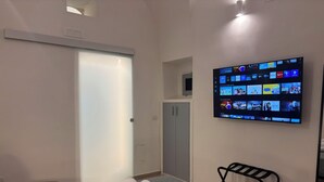 Habitación de hotel con cama, televisor montado en la pared mostrando varios canales, armario y una mesita con toallas.