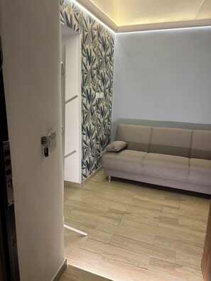 A modern living room with a sofa, patterned wallpaper, and a wooden floor.