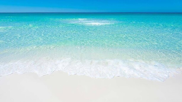 Une plage à l’eau turquoise et au sable blanc.