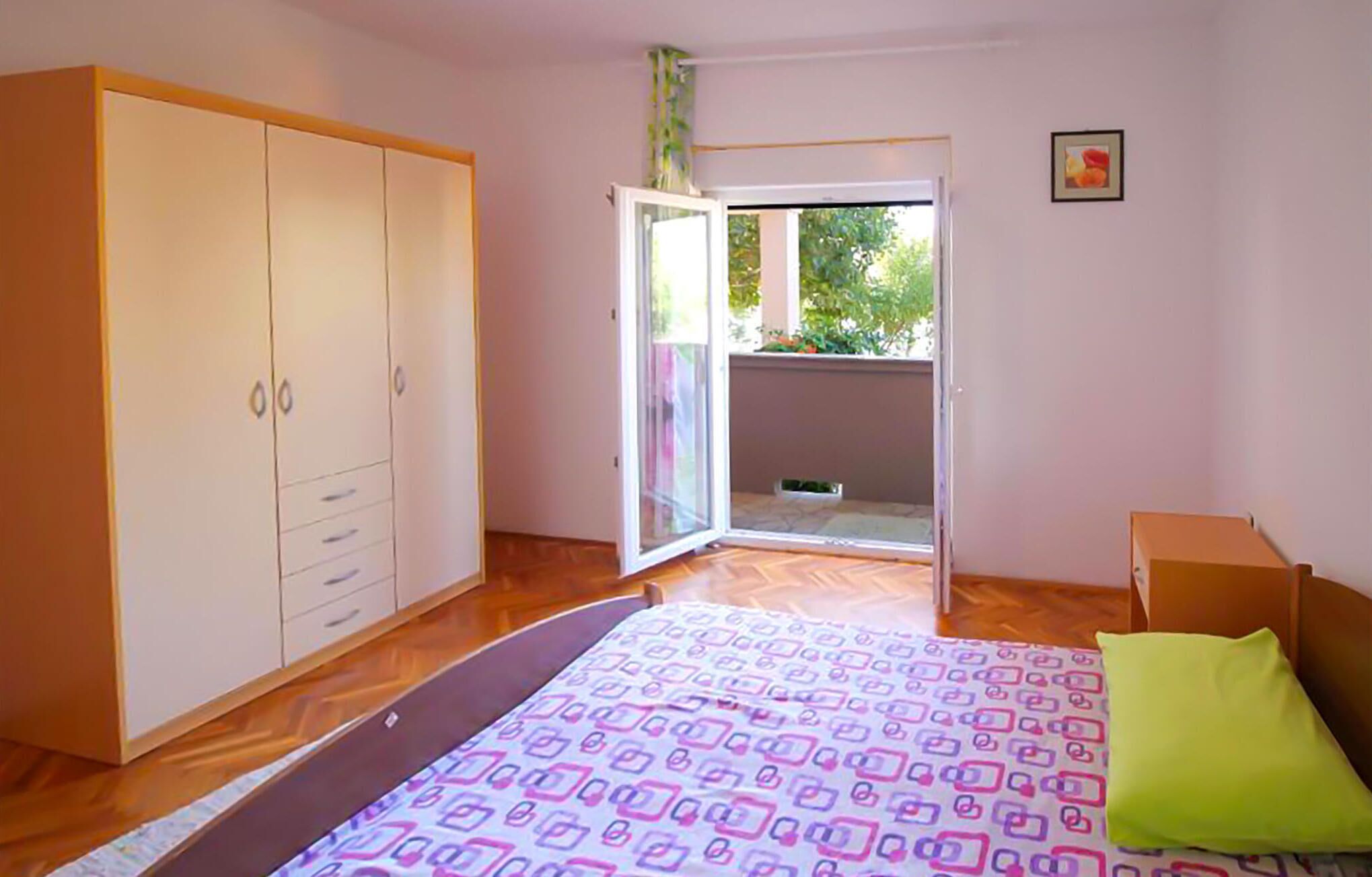 Un dormitorio con cama, armario, puerta corredera a un balcón y una pequeña mesa.