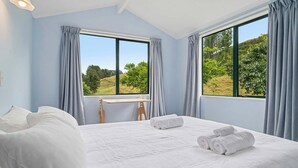 A bedroom with a large bed, a desk, and a view of greenery outside. - Whare Marie - Direct Redwoods Trail Access! (Rotorua)
