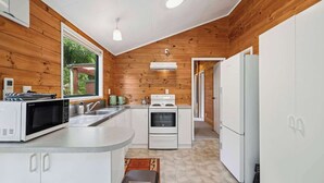 A compact kitchen with white cabinets, a microwave, a stove, and a refrigerator. - Whare Marie - Direct Redwoods Trail Access! (Rotorua)