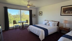 A hotel room with a bed, a desk, a chair, a window with curtains, and a ceiling fan.