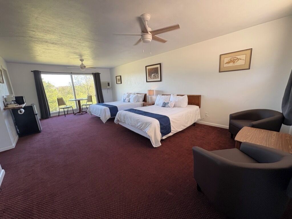 A hotel room with two beds, a desk, a chair, a ceiling fan, and a window with curtains.