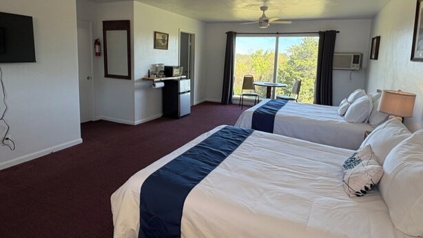 A hotel room with two beds, a desk, a chair, a television, and a view of the outdoors.