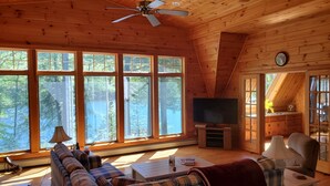 A cozy cabin interior with a large window, a ceiling fan, a television, and a plaid sofa. - Stunning Belgrade Lakes Waterfront Retreat – Dock, Kayaks & Breathtaking Views! (Rome)