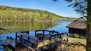 A wooden dock with chairs and a table overlooking a calm lake, surrounded by forested hills. - Stunning Belgrade Lakes Waterfront Retreat – Dock, Kayaks & Breathtaking Views! (Rome)