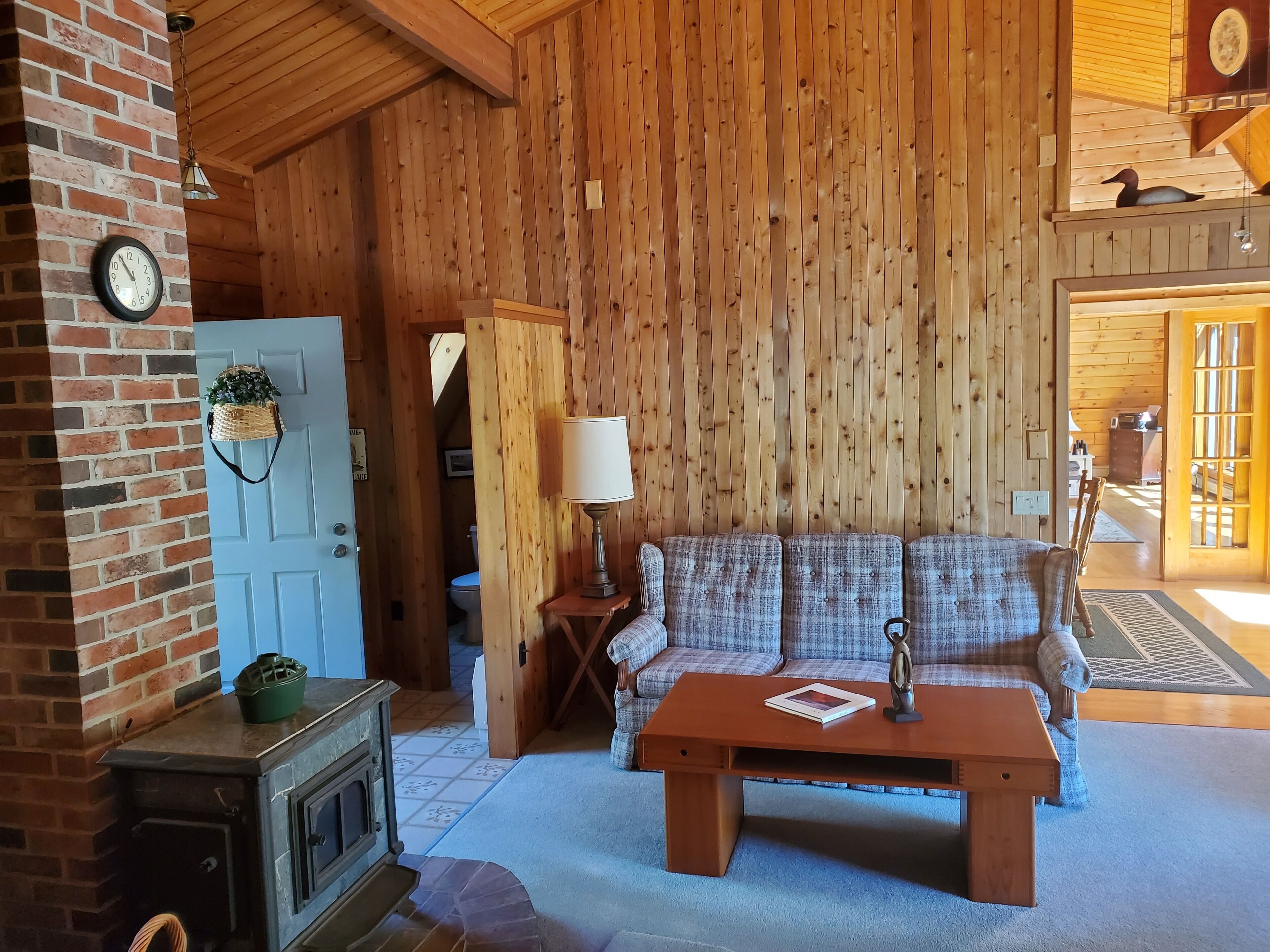 A cozy cabin interior with a wooden wall, a blue door, a fireplace, a sofa, and a lamp.