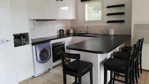 A modern kitchen with a central island, built-in appliances, and black bar stools. - Les Calanques, one-bedroom apartment with air conditioning, large terrace and elevator (Cavalaire-sur-Mer)