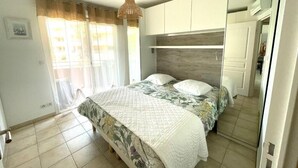A bedroom with a bed, curtains, a hanging light fixture, and a wardrobe. - Les Calanques, one-bedroom apartment with air conditioning, large terrace and elevator (Cavalaire-sur-Mer)