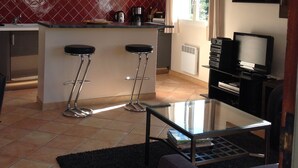 A compact kitchen with a central island, two bar stools, a dining table, and a television. - A cozy little house in the vineyards, in a quiet setting, just a 1/4 walk from the beach—3 minutes by car! (Cassis)