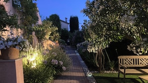A paved garden pathway with potted plants and a bench.