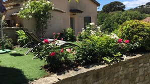 A house with a garden, a patio with a table and chairs, and a stone wall. - A cozy little house in the vineyards, in a quiet setting, just a 1/4 walk from the beach—3 minutes by car! (Cassis)