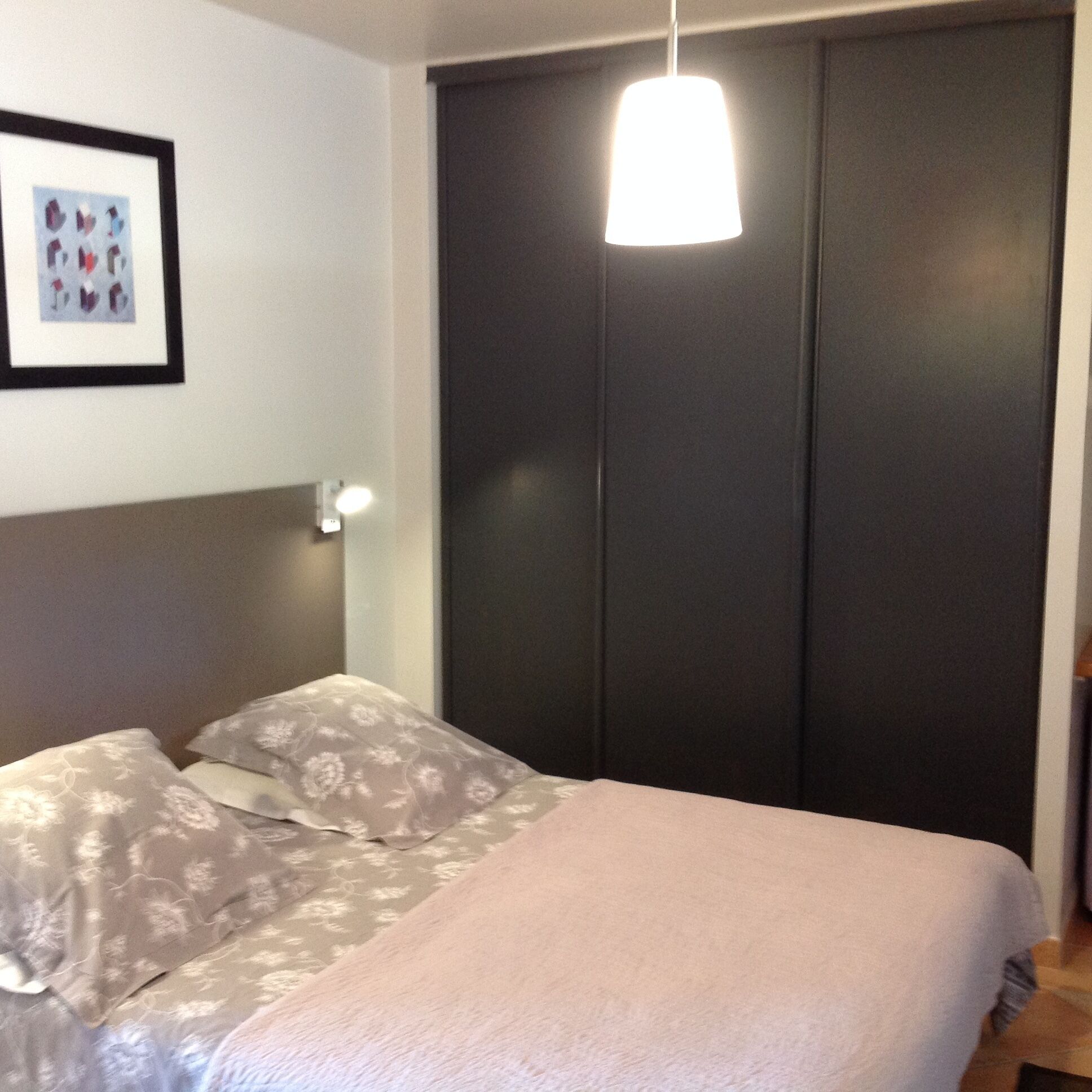 Une chambre à coucher avec un lit, une table de chevet, un tableau encadré au mur et un placard.