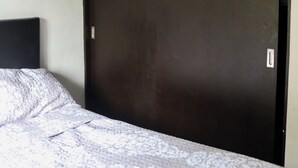 Une chambre à coucher avec une grande armoire en bois sombre, une couvre-lit à motifs et un mur uni.
