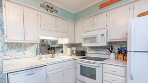 Una cocina con armarios blancos, microondas, estufa y lavavajillas.