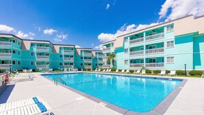 Una piscina con sillas de descanso y un edificio de varios pisos con balcones.