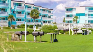 Un hotel frente a la playa con edificios de varios pisos, parrillas al aire libre y un césped bien cuidado.