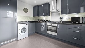 A modern kitchen with grey cabinets, a built-in washing machine, a stove, and a microwave.