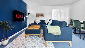 A living room with a blue sofa, a wooden coffee table, a Netflix TV, and a patterned rug.