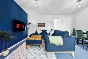 A living room with a blue sofa, a wooden coffee table, a Netflix TV, and a patterned rug. - Spacious Home, Contractors, Super King Beds, Free Parking, Fast Wi-Fi, Netflix (Birmingham)