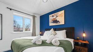 A hotel room with a large bed, a nightstand with a lamp, a window with curtains, and a painting on the wall.