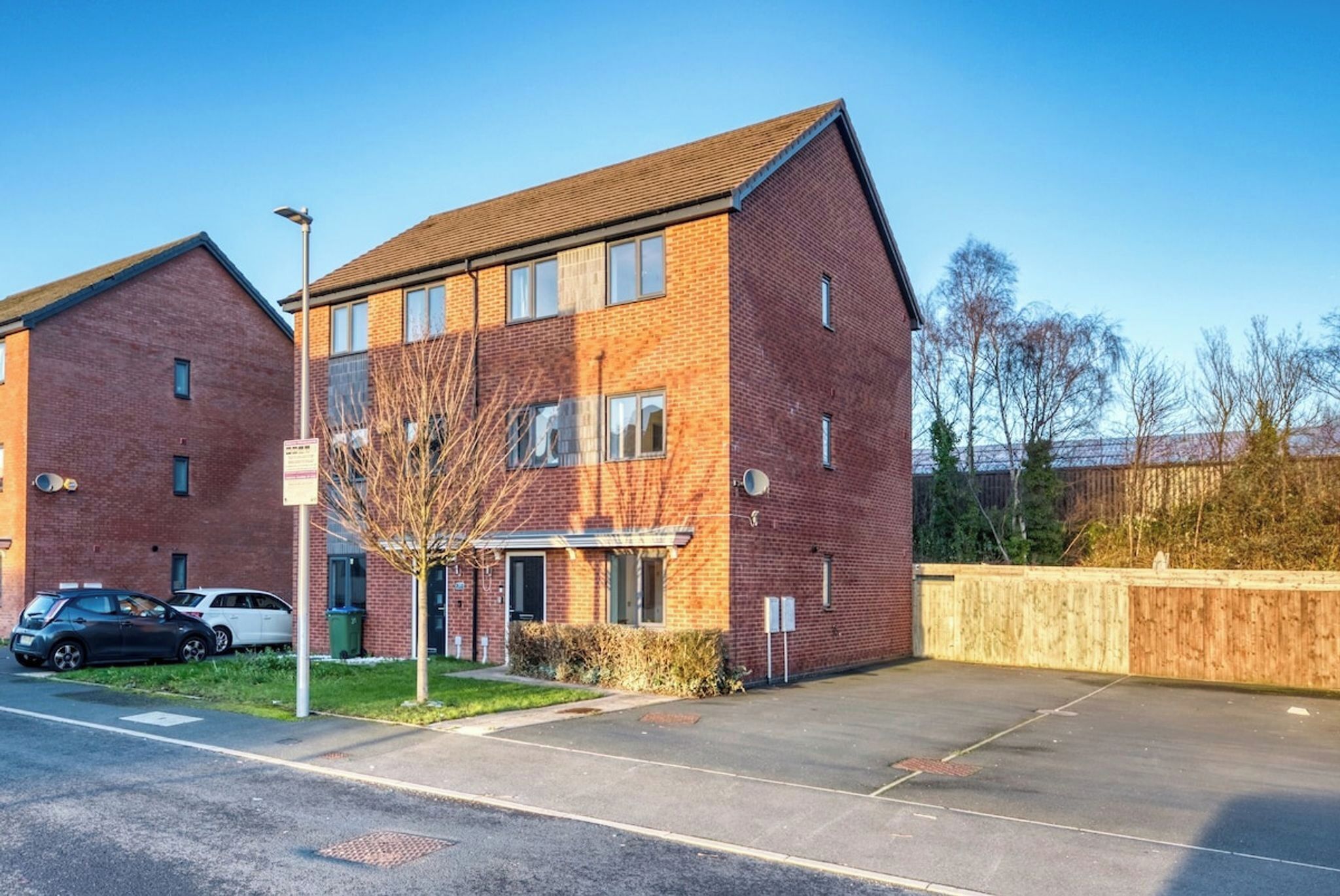 A two-story brick building with a flat roof, a small front garden, and a parking area.