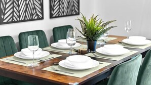 A dining table set with white plates, glasses, and cutlery, surrounded by green upholstered chairs.