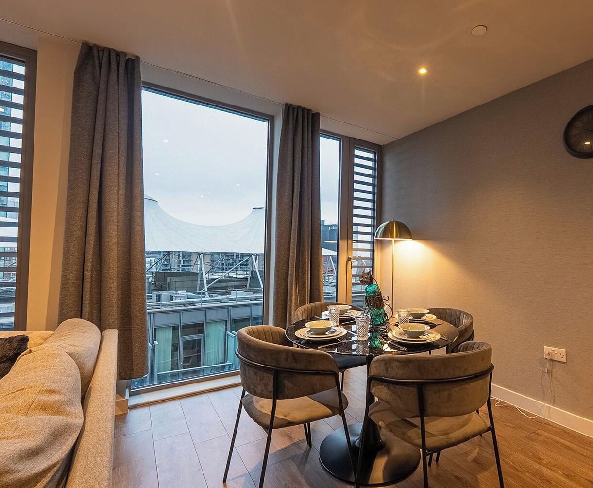 A dining area with a table set for four, a sofa, and a view of the cityscape through large windows.