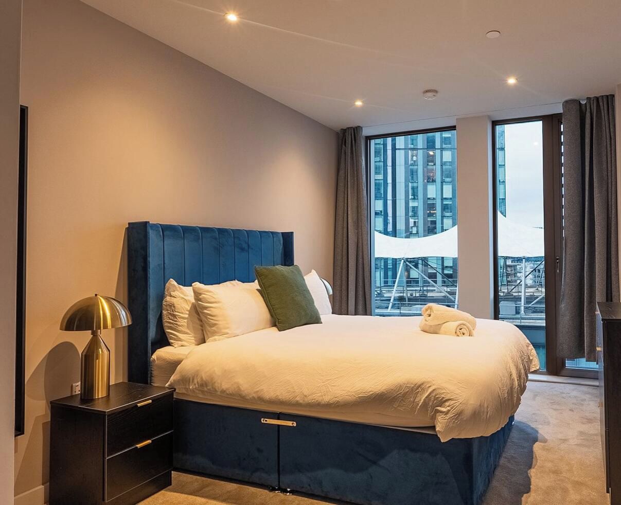 Een moderne hotelkamer met een groot bed, een nachtkastje en een uitzicht op de stad door grote ramen.