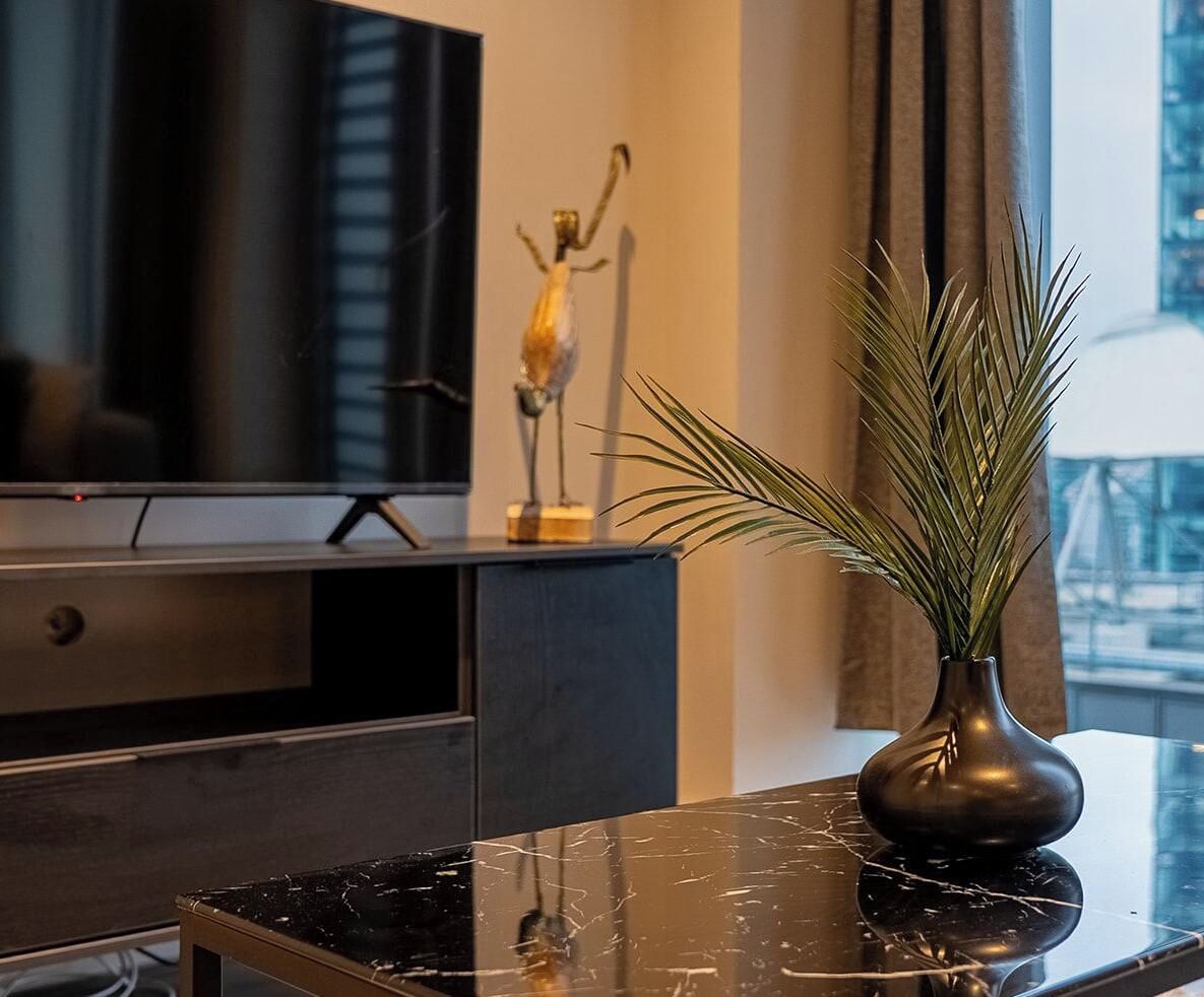 Un salon moderne avec une table basse en marbre, un téléviseur, une sculpture décorative et une plante en pot.