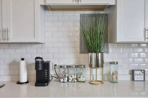 Cucina con mobili bianchi, una macchina da caffè, barattoli con alimenti e una pianta in vaso.