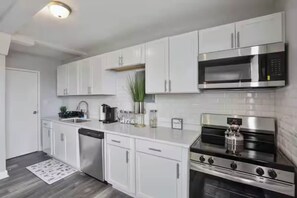 Een moderne keuken met witte kastjes, een roestvrijstalen magnetron, een gasfornuis en een vaatwasser.