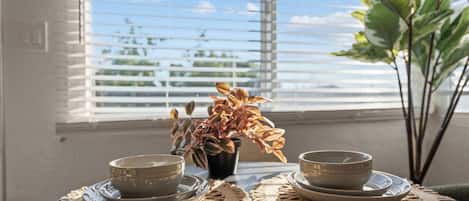 A table with two ceramic bowls and saucers, a woven placemat, and a potted plant with variegated leaves.