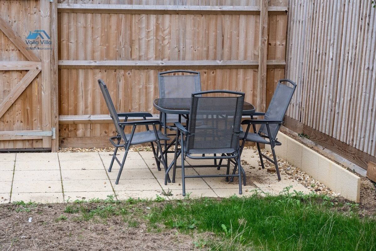 Un espace patio agrémenté d’une clôture en bois, d’une table ronde avec quatre chaises et d’un petit barbecue.